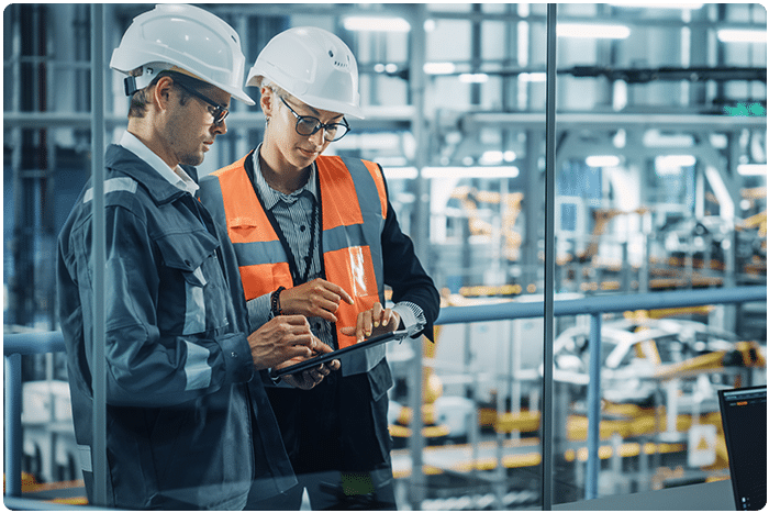 Two workers in hard hats look at safety inspection software on an iPad while in the workplace.